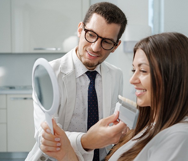 Smiling dentist and patient picking shade of veneer